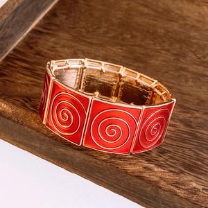 Detail of vintage red enamel square plates on a gold elastic bracelet over wood