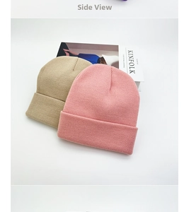 Detail of beige and pink knitted beanies with folded brims on a magazine surface