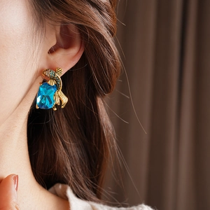 Close-up of a gold fish-shaped earring with a large blue gemstone on a model ear