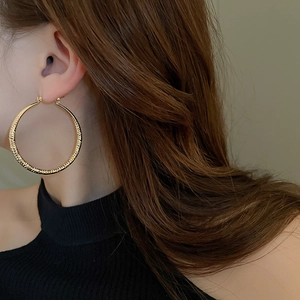 Close-up of large golden hoop earrings with textured diamond pattern on female model