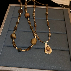 Vue détaillée du collier en œil de tigre avec pendentif goutte dorée sur plateau gris