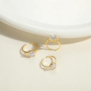 Three gold adjustable rings with square-cut clear crystals on a textured beige surface