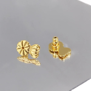 Close-up of golden earring lifters with flower-shaped design on reflective surface