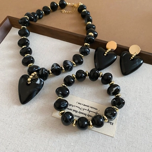 Elegant black and gold heart jewelry set with necklace, bracelet, and stud earrings