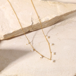 Detail of 18K gold stainless steel chain necklace with tiny white pearls on stone surface