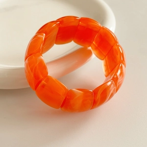 Macro view of orange acrylic geometric stretch bracelet with marble texture on white ceramic