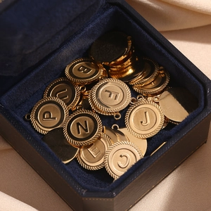 Detailed shot of 18K gold plated round letter pendants with textured edges in velvet box
