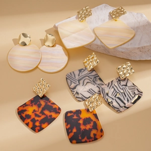 Set of four geometric acrylic earrings with gold hammered texture on a stone background