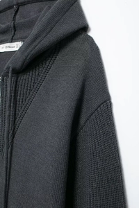 Close-up of dark grey knitted hoodie showing thick textured fabric and neck label