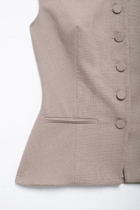 Close-up of light brown plaid vest featuring fine houndstooth texture and button detail