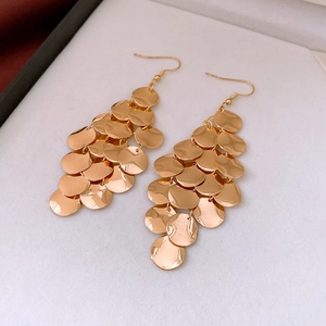 Macro view of gold layered sequin drop earrings on white velvet jewelry box lining