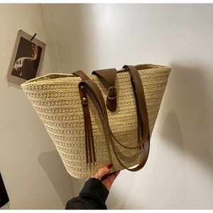 Close-up of beige straw tote bag featuring brown leather straps and buckle detail
