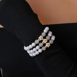 Detailed shot of three-piece acrylic beaded bracelets with gold floral charms on wrist