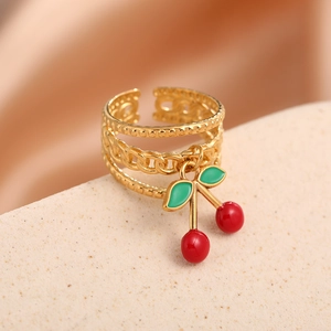 Detail of a multi-layer gold ring featuring a vibrant red and green cherry pendant charm