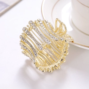 Elegant gold metal hair claw clip with rhinestones and pearls on a white desktop setting