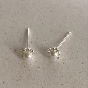 Pair of 925 sterling silver pearl stud earrings with crown setting on beige texture