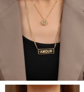 Détail de colliers superposés en titane doré avec pendentifs Double Bonheur et Amour