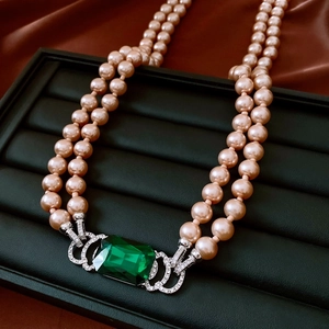 Detail of vintage emerald pendant necklace with pink pearls on black leather tray