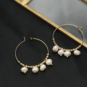 Detail of gold hoop earrings featuring freshwater pearls and small golden beads on black fabric