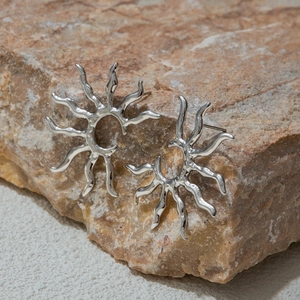 Detailed close-up of silver sun-shaped earrings on a rustic stone with metallic finish