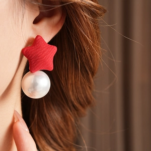 Close-up of red fabric star earrings with white pearl pendants worn by a model