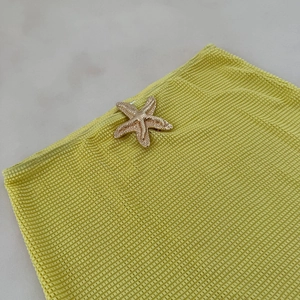 Close-up of golden starfish charm on bright yellow waffle textured bikini fabric