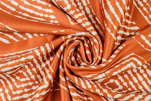 Close-up of orange satin fabric with white geometric dots showing pleated texture and shine