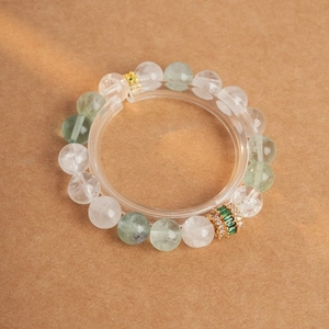 Detail of beaded bracelet featuring clear green beads with gold accents and zircon charm