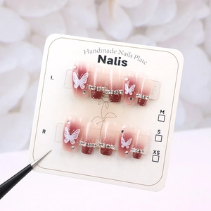 Macro detail of cherry red gradient press-on nails with butterfly and rhinestone accents