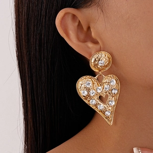 Close-up of oversized hammered gold heart earrings with rhinestones worn by a model