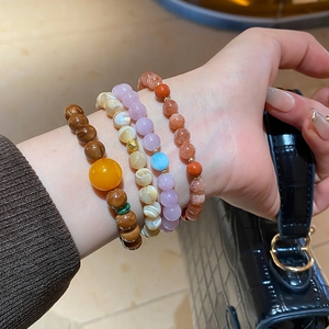 Detailed view of layered beaded bracelets with shell and natural stone on woman's wrist