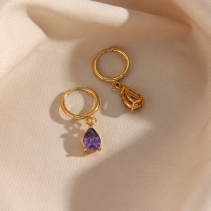 Detalle macro de pendientes dorados con circonita púrpura en forma de lágrima