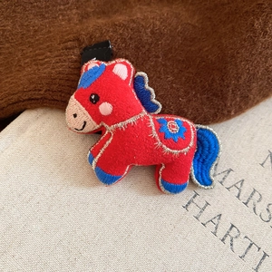 Detailed close-up of a red embroidered horse brooch with blue floral patterns and gold edges
