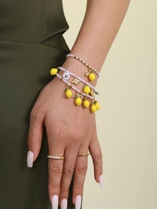 Detail of beaded pearl bracelets with lemon and daisy charms worn with gold rings