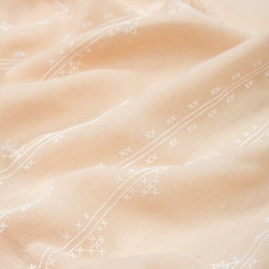 Macro shot of light peach cotton linen fabric with white cross-stitch pattern details