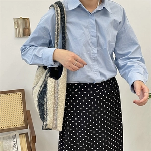 Lifestyle shot of large plush plaid tote bag styled with blue shirt and polka dot skirt