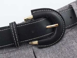 Detail of black leather belt with gold D-ring buckle and contrast white stitching