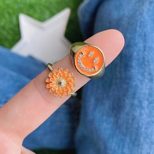 Golden rings with orange enamel smiley face and daisy flower on denim background