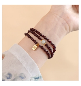 Close-up of triple-wrap garnet bead bracelet with Hetian jade and gold Fu pendant