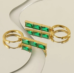 Détail macro de boucles d'oreilles dorées avec zircon vert émeraude sur miroir