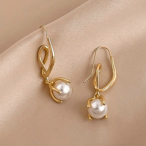 Detail of twisted gold metal earrings with glossy white pearls on beige silk