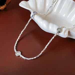 Detail of silver smiley face pendants on a square link chain over a shell dish