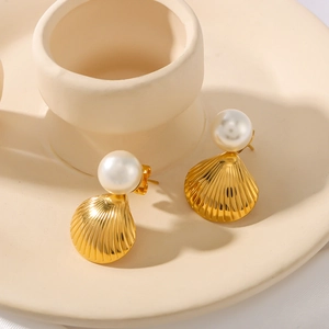 Elegant gold shell stud earrings with white pearls on minimalist ceramic stand