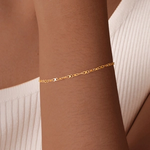 Macro shot of minimalist gold infinity link bracelet worn on a dark skin tone model