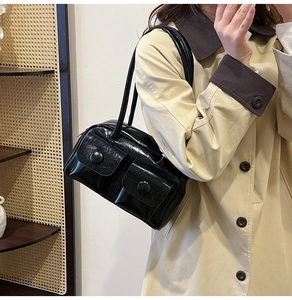 Detail of glossy black shoulder bag with two front flap pockets and circular metal buckles