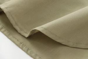 Close-up of precise stitching on olive green poplin shirt hem and fabric texture