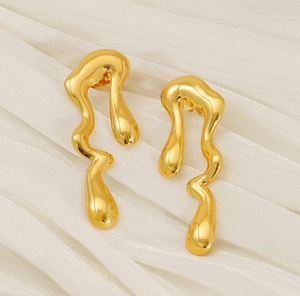 Detailed macro view of gold liquid lava earrings on a soft cream fabric background