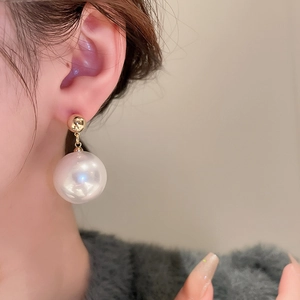 Close-up of gold beaded stud earring with large white pearl drop on female model