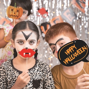 Children holding Halloween photo booth props including pumpkin mask and vampire lips