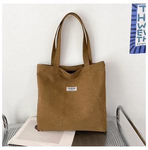 Detail of a brown corduroy tote bag featuring white Fashion Instinct label and sturdy straps